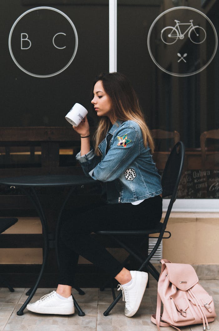 Young woman in denim jacket savoring coffee at a trendy outdoor café.